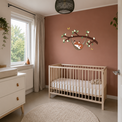 Babykamer met houten ledikant, witte commode en houten wanddecoratie van een slapend vosje in een hangmat aan een tak op roestkleurige muur.
