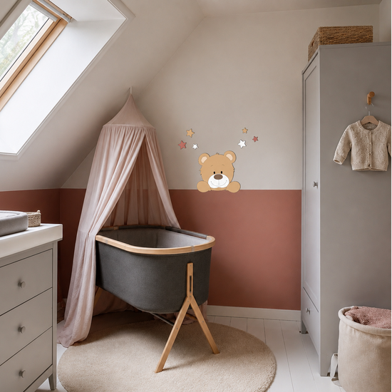 Zolderbabykamer met wieg onder een roze klamboe, terracotta lambrisering en houten muurdecoratie van een beertje met sterren.
