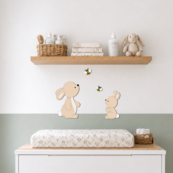 Houten muurdecoratie met moederkonijn, babykonijntje en twee bijtjes boven een commode in een rustige babykamer.