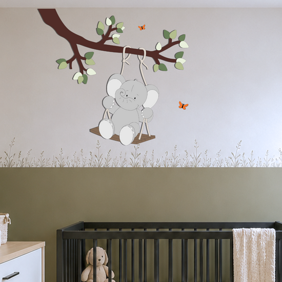 Gezellige babykamer met zwarte meubels en groene lambrisering op de muur. Aan plafond tak met groene bladeren muurdecoratie, met schommelend olifantje eraan.