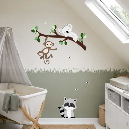 Babykamer met witte plankenvloer en wiegje. Muurdecoratie van tak met aapje en koala en wasbeertje op de plint.