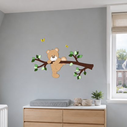 Muurdecoratie kinderkamer donkerbruine tak met groene bladeren en een klauterend beige beertje op muur in oudblauw. 