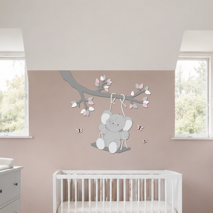 Houten muurdecoratie voor de baby- of kinderkamer met een olifantje op een schommel aan een tak, uitgevoerd in grijstinten met roze accenten, blaadjes en vlinders.