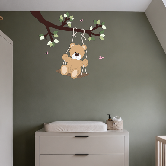 Houten muurdecoratie van tak met schommelend beertje, op donkergroene wand met licht babykamer meubels.
